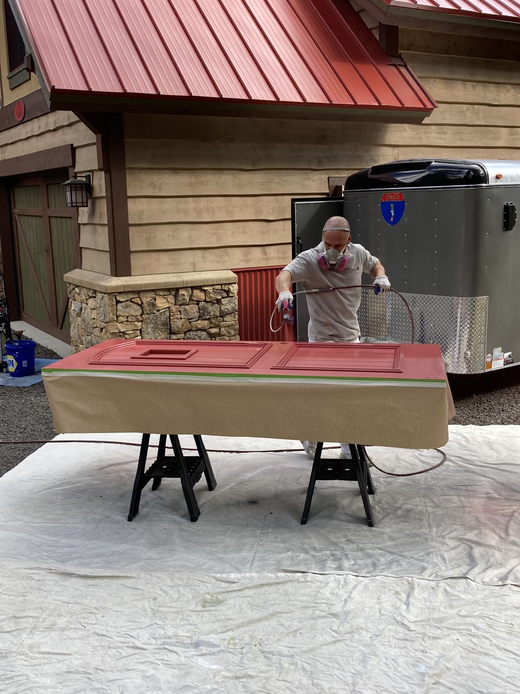 Paul spraying a red door on sawhorses outside a cabin