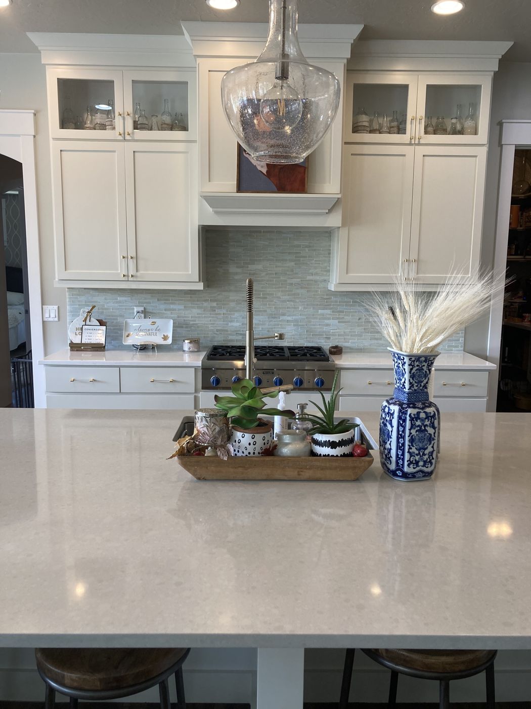 White kitchen cabinets and range hood around a quartz island